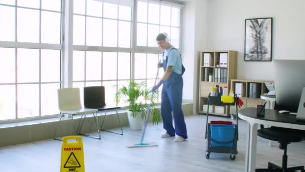 Mies aasialainen talonmies kuuntelee musiikkia moppaamalla lattiaa toimistossa
 - Materiaali, video