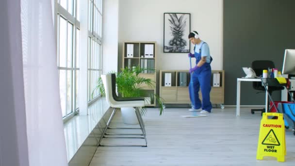 mężczyzna Azji woźny słuchanie muzyka podczas mopping podłoga w biuro - Materiał filmowy, wideo