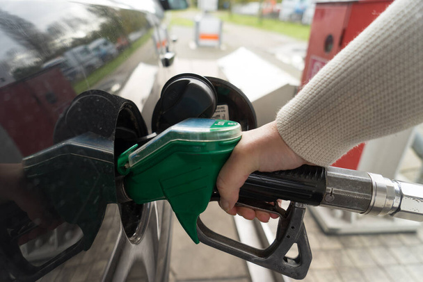 Vrouwelijke hand vullen benzine in een auto met gas pomp mondstuk - Foto, afbeelding