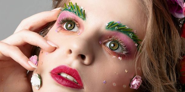Portrait of a beautiful girl with creative make-up. Summer girl. The face of a luxurious model in flowers. The concept of eyebrow and eyelash extensions. - Fotoğraf, Görsel