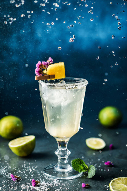 Cocktail de limonade fraîche avec citron vert, menthe et glace dans un verre à vin sur fond bleu foncé. Prise de vue studio de boisson en mouvement de gel, gouttes volantes dans éclaboussure liquide. Boisson froide et cocktail d'été
 - Photo, image