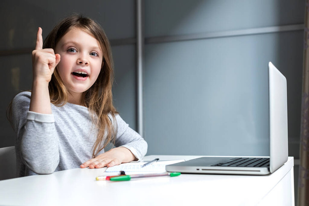 Egy gyerek érzelmei az online órákon. Okos lány ül az iskolaasztalnál egy laptoppal. Felkiáltójel. - Fotó, kép