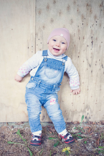Gelukkig glimlachend meisje met roze pet en jeans tuinbroek achterover leunend op de muur. Prachtig geluk en jeugd. Eerste stap - Foto, afbeelding