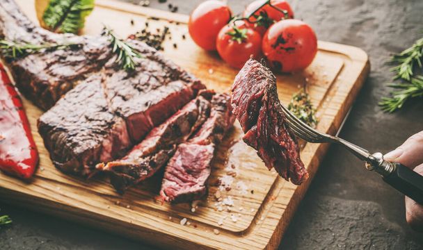 Kézzel vágott grillezett tomahawk hús közepes ritka vagy borda szem steak fa vágódeszka grillezett zöldség sötét alapon, közelről, tonizálás - Fotó, kép