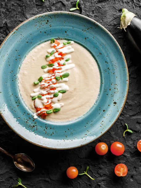 Kremowa zupa bakłażana ze śmietaną, pomidorami, cukinią i kiełkami w talerzu na ciemnym tle. Zdrowe wegańskie jedzenie, czyste jedzenie, dieta, widok z góry - Zdjęcie, obraz