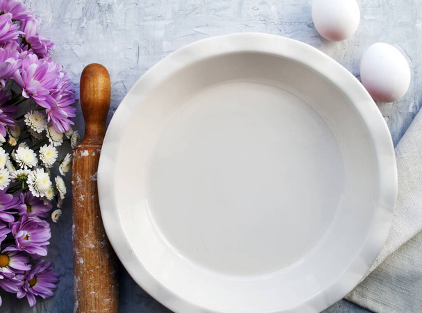 Lege plaat voor taart, eieren, deegroller en een boeket bloemen. Het concept van het proces van het koken taart, taart. - Foto, afbeelding