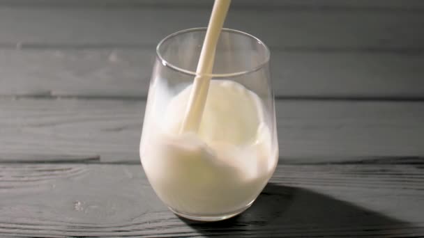 Pouring of fresh milk in glass on wooden background - Imágenes, Vídeo