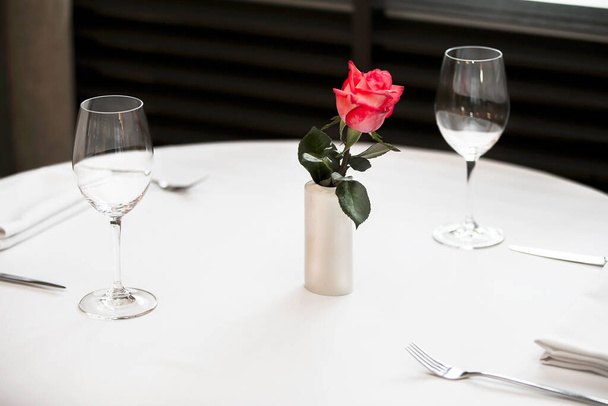 White table with glasses and cutlery. Empty restaurant table with red rose. - 写真・画像