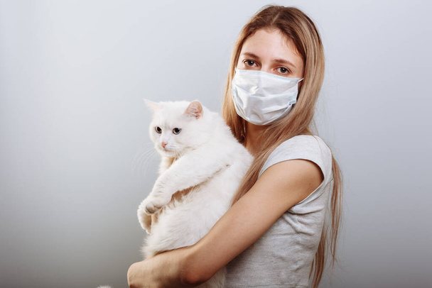 Frau in Schutzmaske hält Katzenhaustier in Gesichtsmaske. Chinesische Coronavirus-Krankheit COVID-19 ist gefährlich für Haustiere. - Foto, Bild