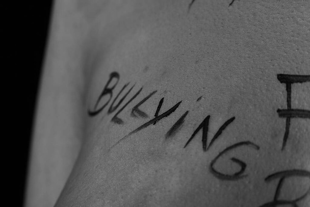 egy fiatal lány testrésze, akit zaklattak a feliratokkal. A feliratok a fotós kezébe vannak írva, nem egy tetoválásba. fekete-fehér fénykép. - Fotó, kép
