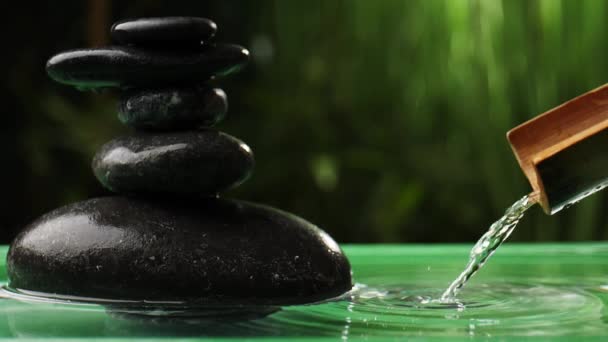 Água que despeja de bambu em lago com pilha de pedras zen no jardim oriental
 - Filmagem, Vídeo