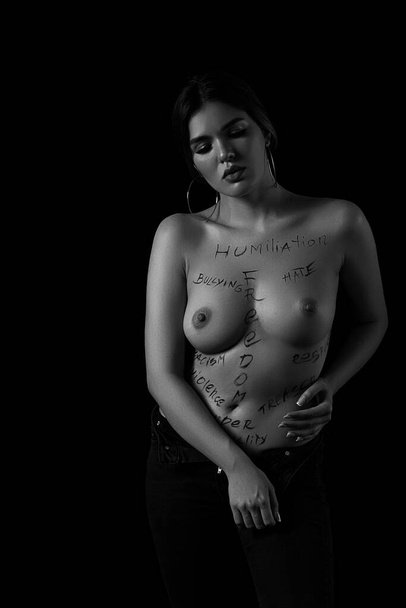 ασπρόμαυρο πορτραίτο ενός νεαρού κοριτσιού με τις λέξεις ταπείνωση, εκφοβισμός, μίσος, ελευθερία, ανισότητα των φύλων στο γυμνό της σώμα. Οι λεζάντες είναι γραμμένες στο χέρι του φωτογράφου, όχι σε τατουάζ. . - Φωτογραφία, εικόνα