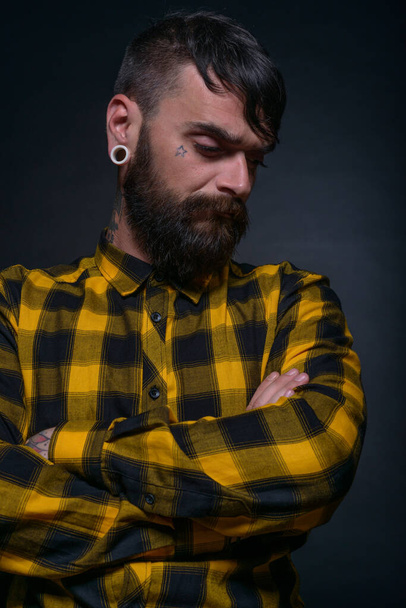Zbliżenie portret brodatego mężczyzny z tatuażami na rękach i szyi w żółtej czarnej koszuli. - Zdjęcie, obraz