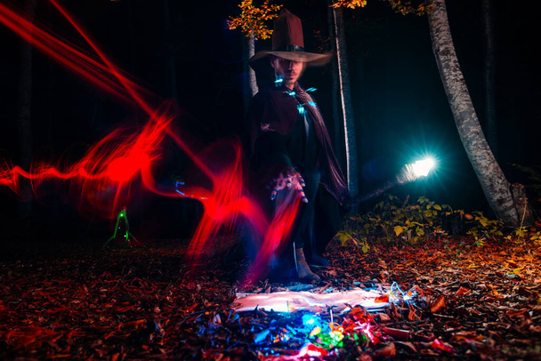 Mago (mago) lanzando un hechizo con su bastón mágico mientras está de pie en un bosque encantado. - Foto, imagen