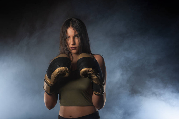 Retrato de close-up de uma boxeadora posando com luvas de boxe e olhando para a câmera com um fundo esfumaçado - Foto, Imagem