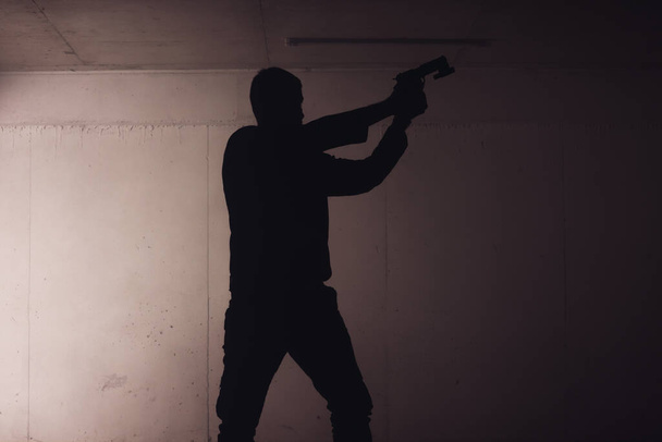 η σιλουέτα ενός οπλισμένου άνδρα που κρατάει το όπλο του και σημαδεύει με την ακτίνα λέιζερ του έναν στόχο. - Φωτογραφία, εικόνα