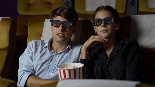 Man and woman in the cinema watching a movie with 3D glasses. with interest looking at the screen, exciting and eating popcorn - Fotografie, Obrázek