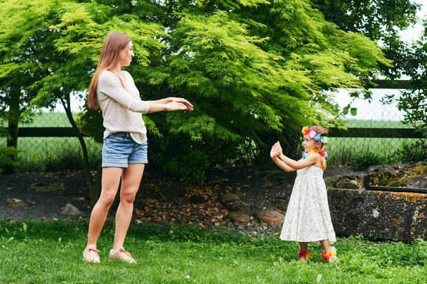 Nuori äiti tanssii söpö pieni tytär puutarhassa, perhe viettää aikaa yhdessä
 - Valokuva, kuva