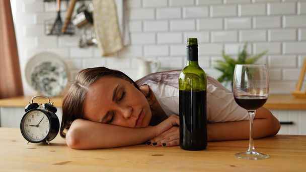 An alcoholic woman sleeps in the kitchen in the morning, near a bottle of wine. - 写真・画像