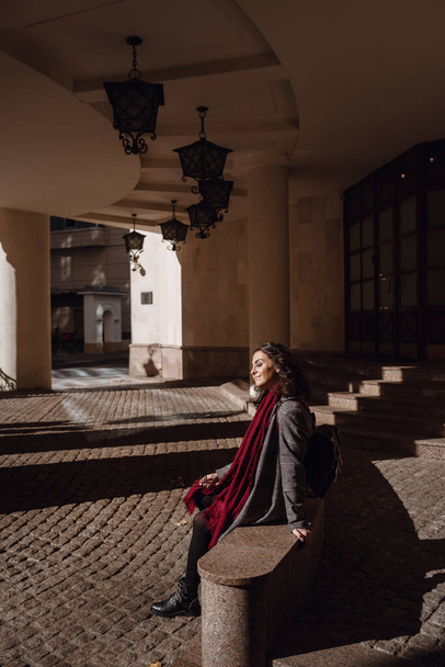 Retrato de outono ao ar livre de jovem elegante menina encaracolado sorridente feliz vestindo casaco cinza, com mochila de couro vermelho, posando na rua da cidade europeia. Copiar, espaço vazio para texto
 - Foto, Imagem