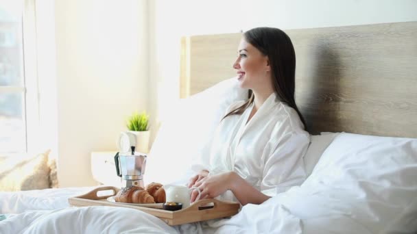 Morning of beautiful young woman having breakfast in bed - Кадри, відео
