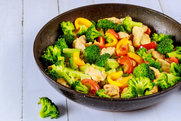 Smaczne zdrowe warzywa smażyć z kurczaka na patelni na białej drewnianej powierzchni. - Zdjęcie, obraz