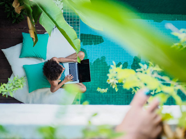 mulher trabalhando online com laptop sentado em uma piscina de água azul
 - Foto, Imagem