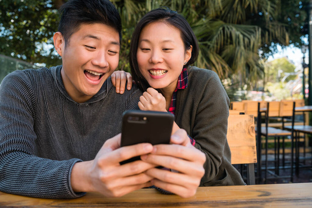 Portrait of lovely asian couple looking at the mobile phone while sitting and spending time at the coffee shop. Love and technology concept. - 写真・画像