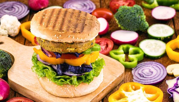 vegetarian burger, home made. with vegetables, fiber and proteins. Gourmet snack with vegetables in the background on a rustic wooden table. - Foto, imagen