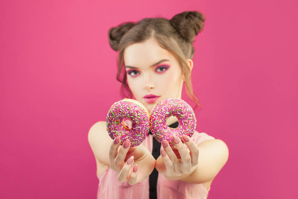 Beautiful fashion woman holding donut on vivid pink background - Foto, afbeelding