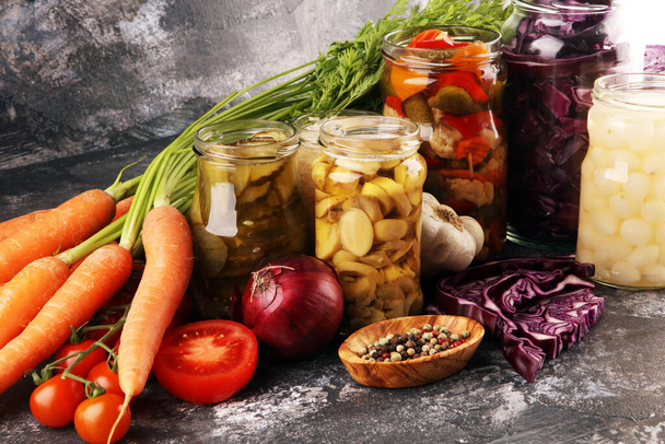 Preserves vegetables in glass jars. Pickled Cucumber, carrot, fermented cabbage and onions on rustic table - 写真・画像