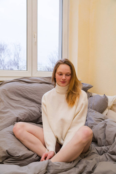 Girl in warm sweater sits in lotus position on bed - Foto, Imagem