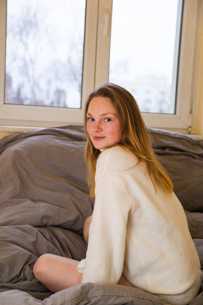 Soft photo of woman on bed wearing knitted sweater - 写真・画像