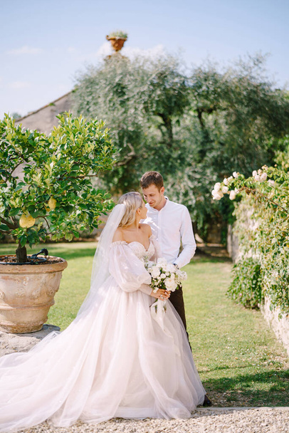 Esküvői pár a kertben. A vőlegény megöleli a menyasszonyt a citromfák mellett. Esküvő Firenzében, Olaszországban, egy régi villa-pincészetben. - Fotó, kép