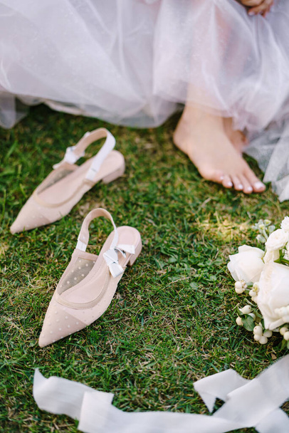 Bare feet of the bride on the grass, next to shoes and a bouquet. Wedding in Florence, Italy, in an old villa-winery. - Photo, Image