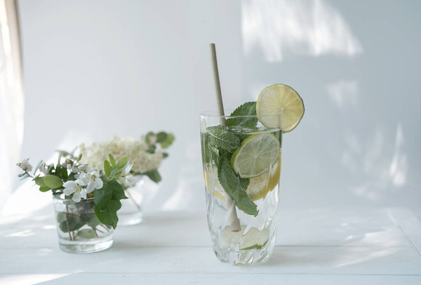 παγωμένο ποτήρι μοχίτο. lime, λεμόνι, φύλλα δυόσμου σε ένα ψηλό ποτήρι. μοντέρνο άμεσο ηλιακό φως. μη αλκοολούχο κοκτέιλ το καλοκαίρι. - Φωτογραφία, εικόνα