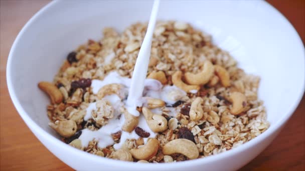 The concept of breakfast, a healthy diet, granola with cashew nuts and slices of raspberries and raisins. Slow motion milk pouring in bowl of muesli breakfast cereals. Healthy food - 映像、動画