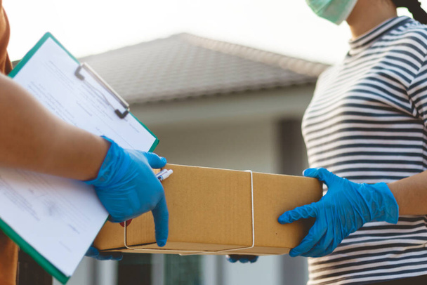 A postás viseli a védőkesztyűt Szállítsa haza. Ázsiai nő kap dobozokat postás. Postás ad. Maradj otthon koncepció.. - Fotó, kép