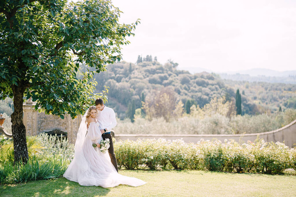 Mariage à Florence, Italie, dans une ancienne villa-cave. Mariée et marié à l'ombre d'un arbre. Couple de mariage marche dans le jardin
. - Photo, image