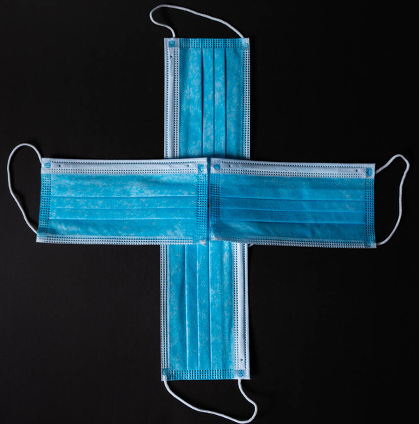 Vier chirurgische Gesichtsmasken als Kreuz vor schwarzem Hintergrund zusammengesetzt - Foto, Bild