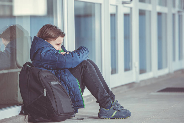 Маленький мальчик или ребенок, сидящие в одиночестве на полу перед школой после того, как пострадали от издевательств
 - Фото, изображение