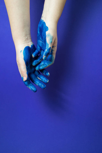 Two artist's hands in bright blue paint on blue background - 写真・画像