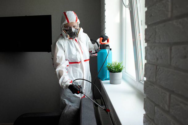Controlo de pragas. Desinfecção de instalações contra insetos e roedores por meios químicos, um trabalhador sanitário com um spray no fundo do apartamento
 - Foto, Imagem