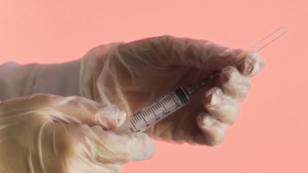 Médico segurando seringa e agulha aberta em um fundo rosa Corona. Covid-19
 - Filmagem, Vídeo