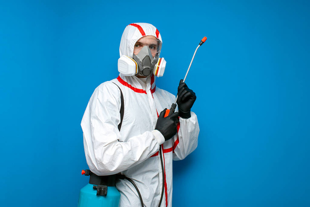 portrait of worker in chemical protective suit with spray gun on blue isolated background, disinfectant with cleaning agent - Photo, Image