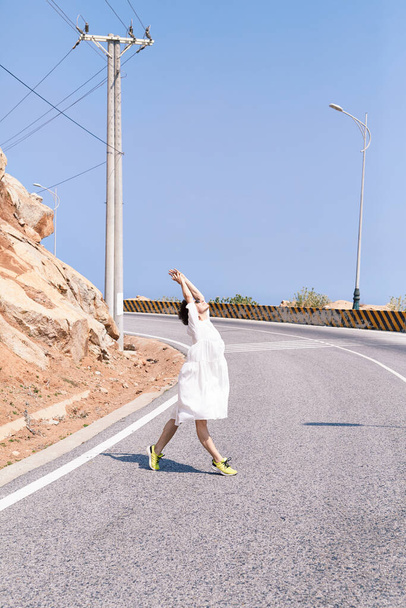 山に走るアスファルトの道路上の白いドレスを着た美しいスポーツ少女 - 写真・画像