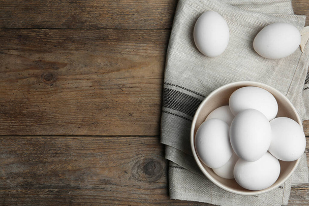 Many fresh raw chicken eggs in bowl on wooden table, flat lay. Space for text - Foto, Imagem