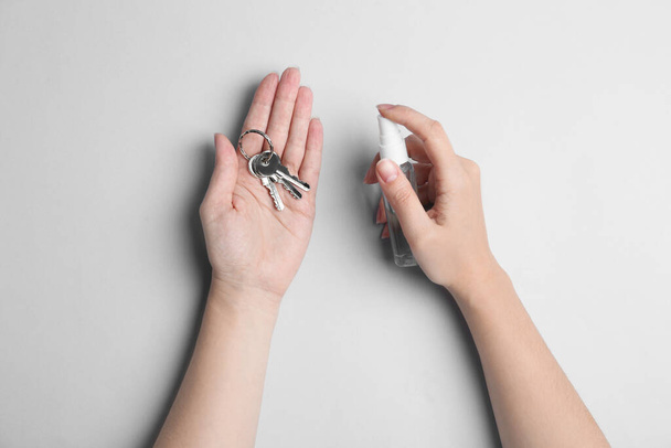 Woman spraying antiseptic onto keys on light grey background, top view - Foto, Imagen