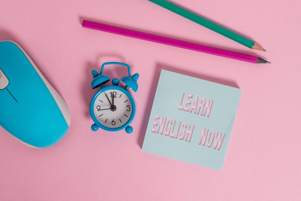 Text sign showing Learn English Now. Conceptual photo gain or acquire knowledge and skill of english language Alarm clock wakeup blank notepad mouse markers colored background. - Photo, Image