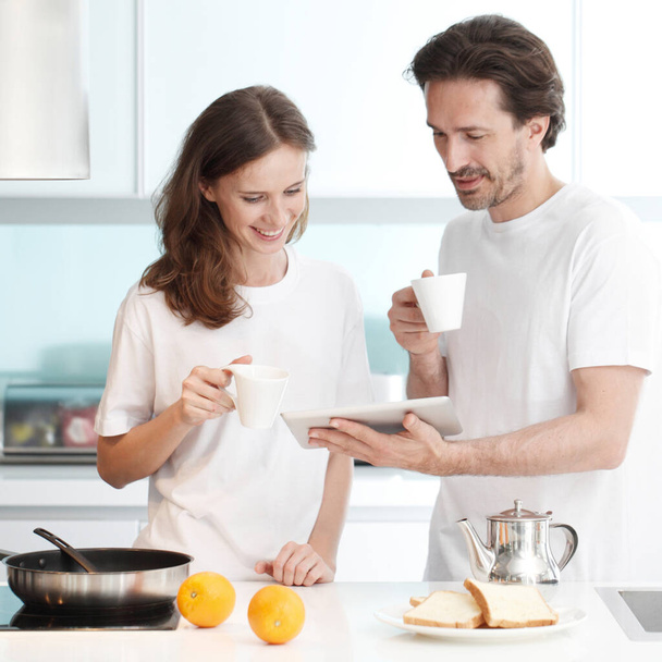 Couple cooking breakfast together in kitchen using tablet pc - Fotó, kép